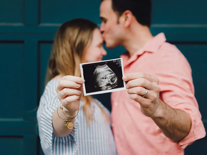 A man and woman holding up a baby ultrasound.