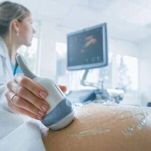 A woman is using an ultrasound machine on her stomach.