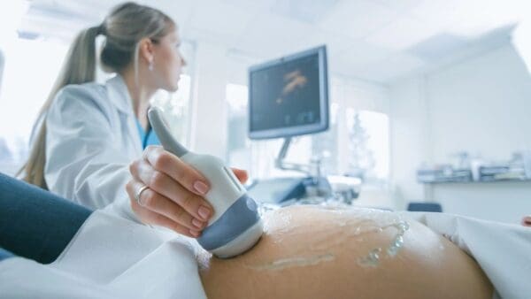 A woman is using an ultrasound machine on her stomach.